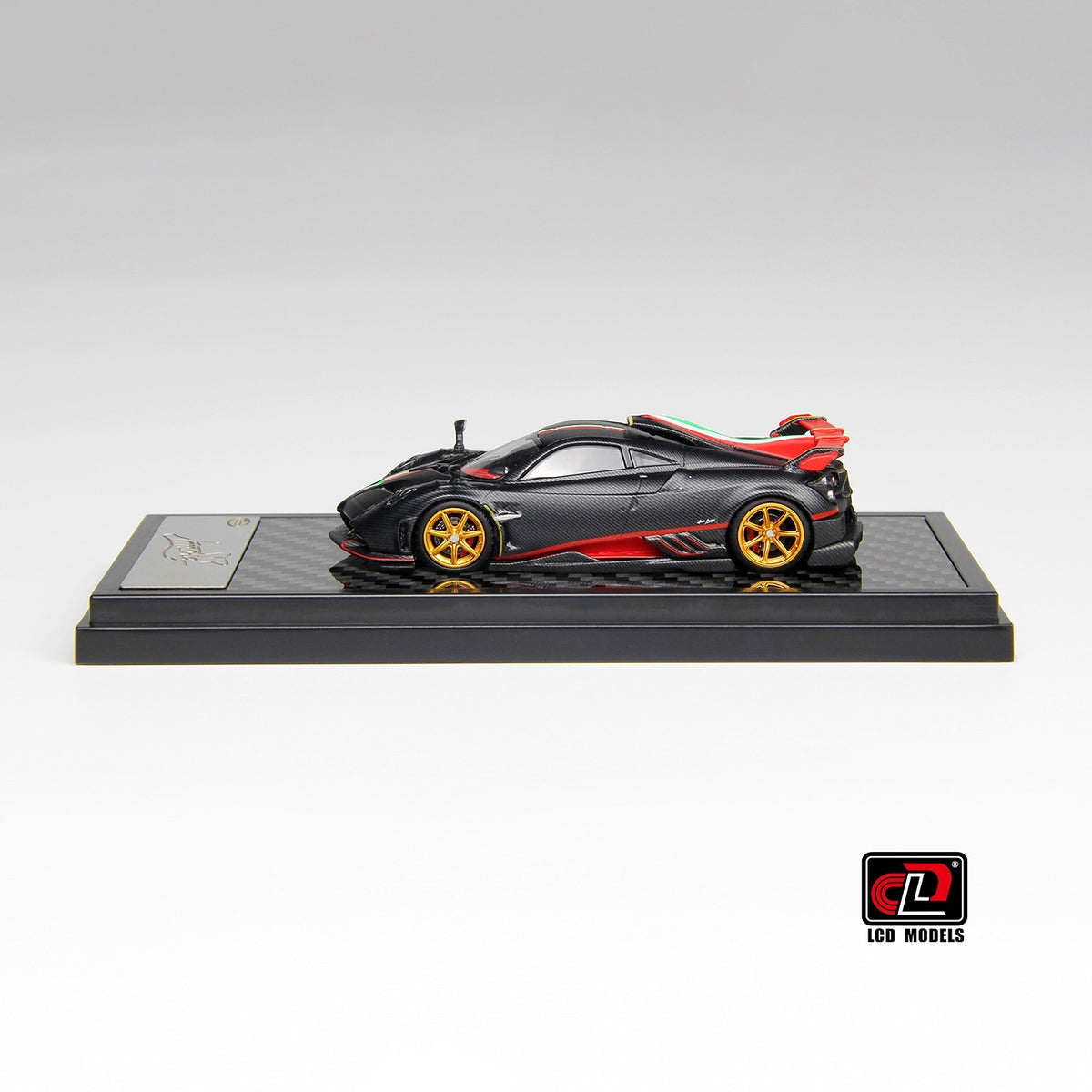 Side profile of Pagani Imola matte carbon 1:64 scale model car showing the red sill accent line and gold multi-spoke wheels (LCD64041-MBCI)